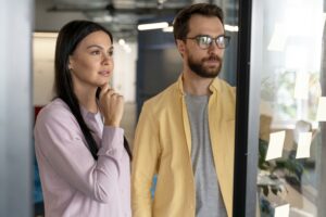 Couple réfléchissant à un achat immobilier en 2025 devant une vitrine d’agence.