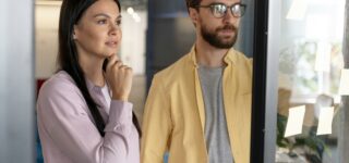 Couple réfléchissant à un achat immobilier en 2025 devant une vitrine d’agence.