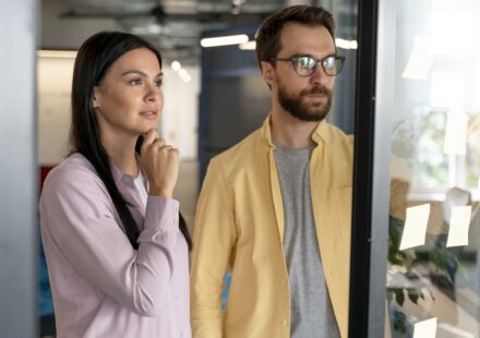 Couple réfléchissant à un achat immobilier en 2025 devant une vitrine d’agence.