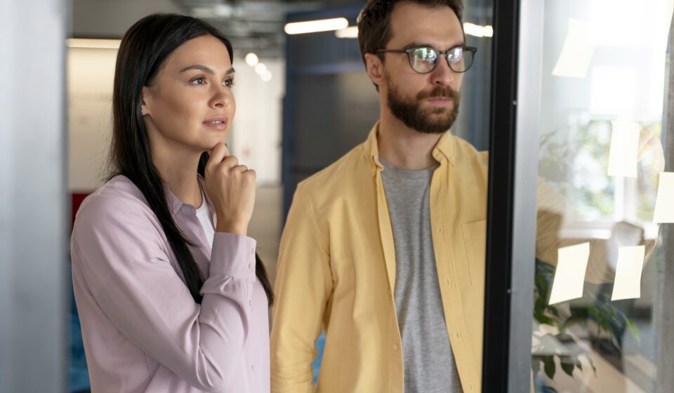 Acheter ou attendre ? Les experts répondent pour la rentrée 2025 Couple réfléchissant à un achat immobilier en 2025 devant une vitrine d’agence.
