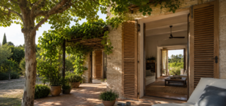 Maison en pierre protégée de la chaleur par des volets, un grand arbre et une pergola végétalisée