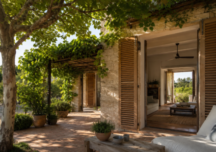 Maison en pierre protégée de la chaleur par des volets, un grand arbre et une pergola végétalisée