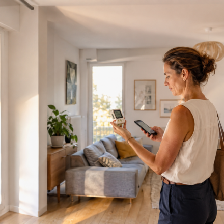 Immobilier et Canicule : comment mesurer la température réelle d’un logement avant de l’acheter ? Acquéreuse mesurant la température intérieure d’un appartement pendant une visite immobilière